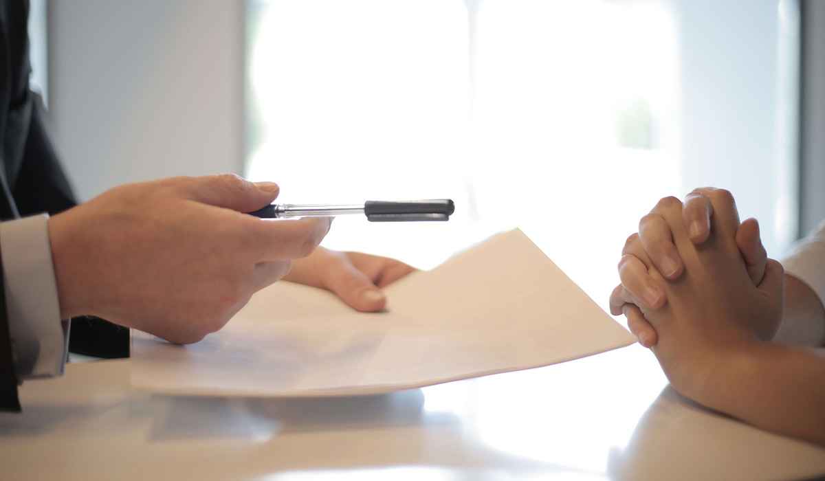 Man sitting on a table holding white papers and a pen 