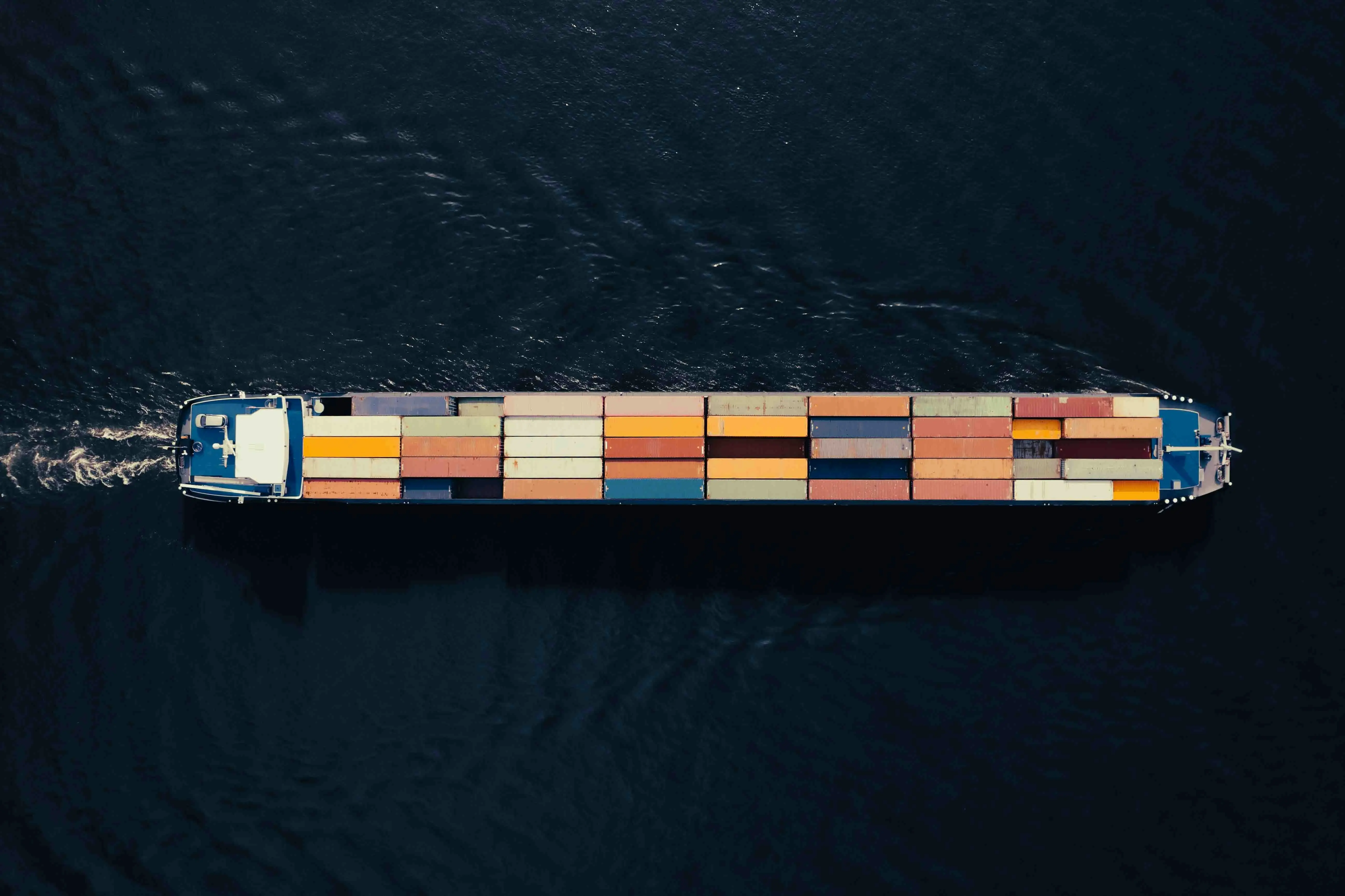 Aerial view of a large container ship carrying stacked cargo containers across open water.
