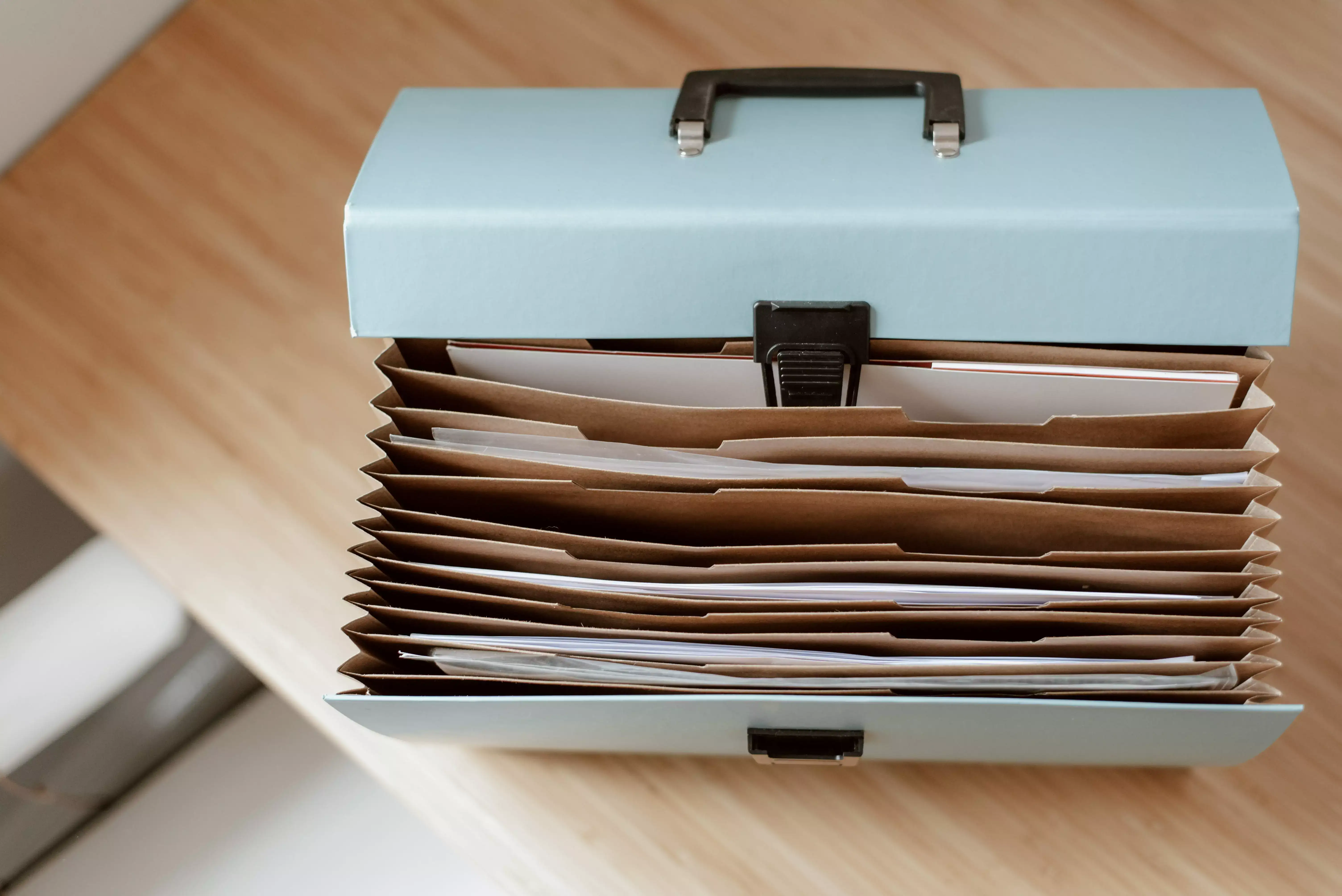 Open accordion file organizer with multiple labeled compartments holding documents and papers on a wooden desk.