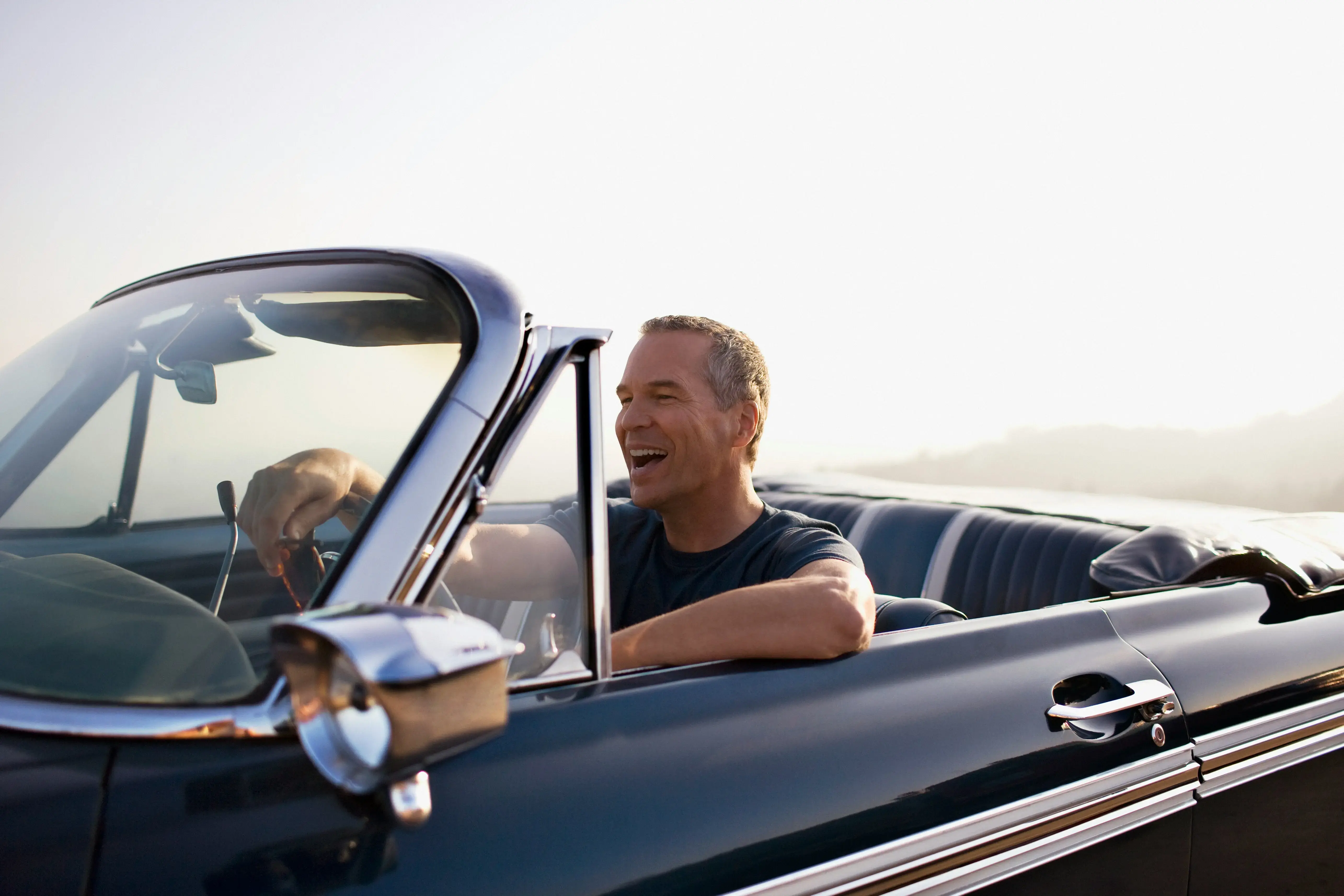 A smiling man driving a classic convertible on a sunny day.